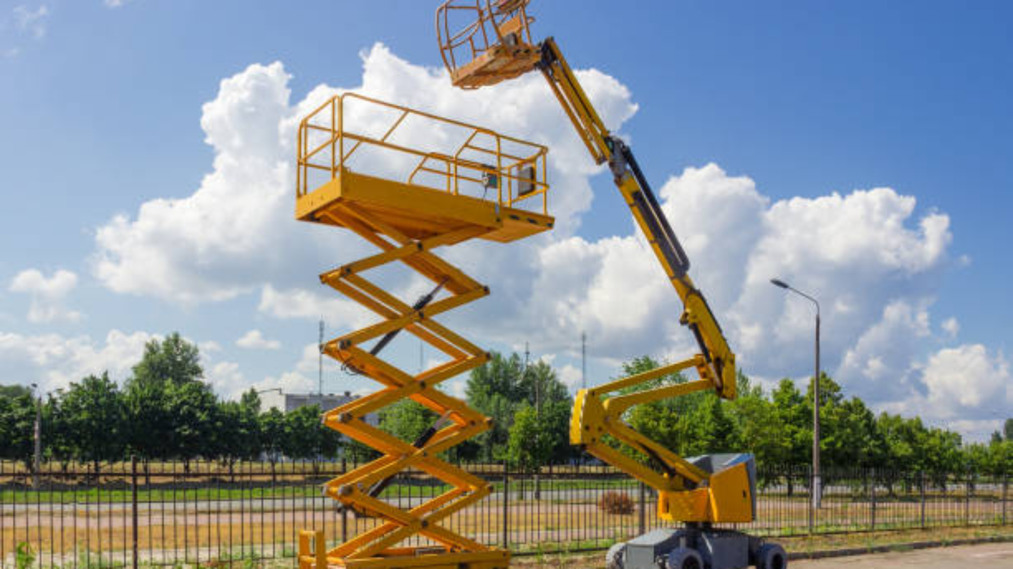 Yellow self propelled articulated boom lift and scissor lift on background of street with trees and sky